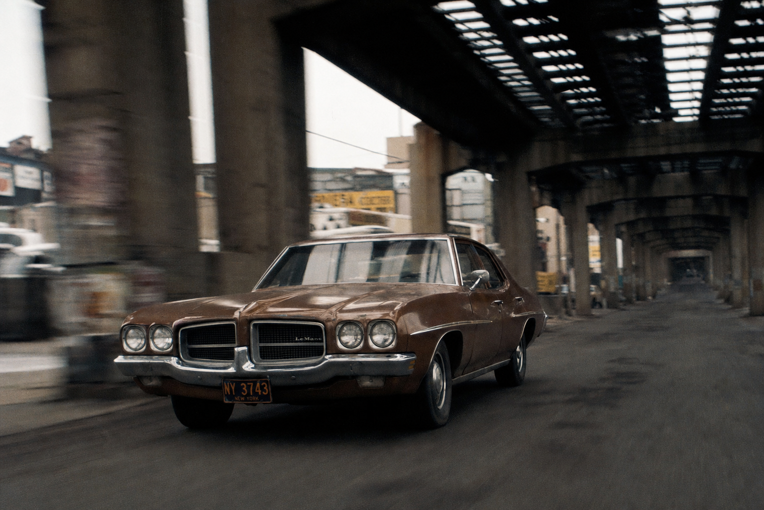 A 1971 brown Pontiac LeMans racing beneath the Brooklyn elevated railway structure