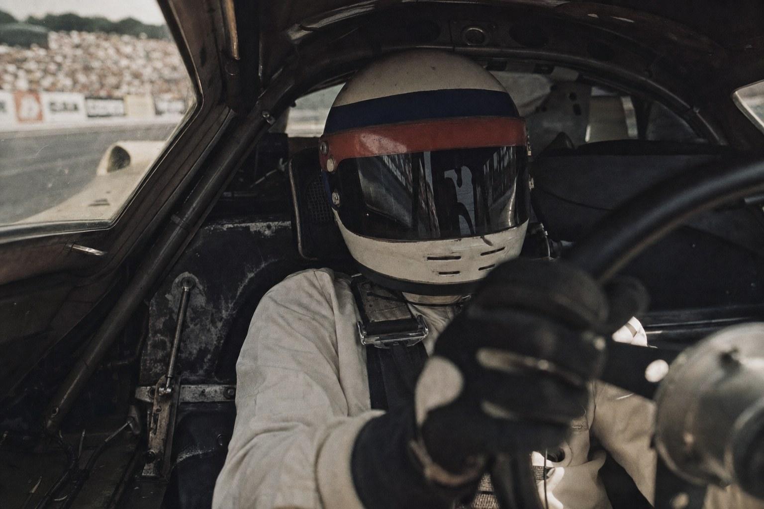 An anonymous helmeted racing driver in the cockpit of a Porsche 917, visor closed, hands on the wheel