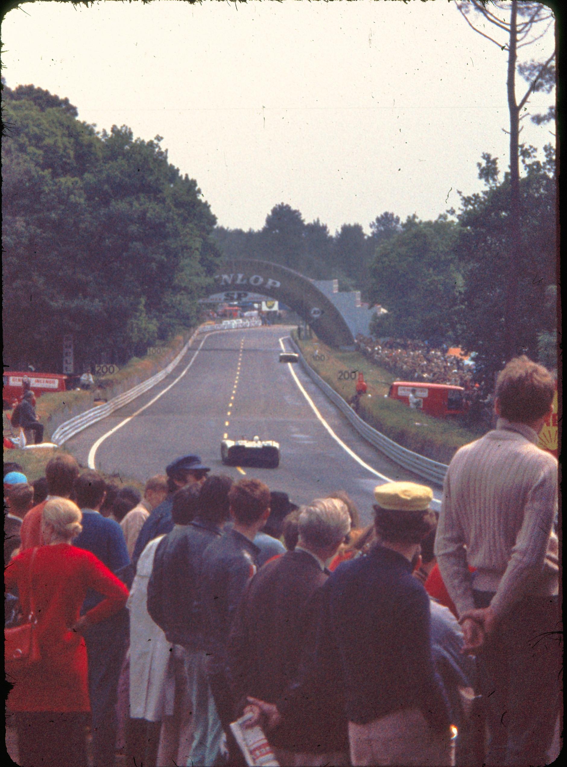 Racing car approaching at speed past the Dunlop Bridge grandstands, Le Mans 1970
